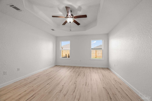 spare room featuring visible vents, a textured wall, light wood finished floors, and a tray ceiling