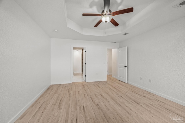 unfurnished bedroom featuring visible vents, a raised ceiling, and light wood-style floors