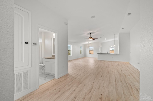 unfurnished living room featuring ceiling fan, visible vents, a textured wall, and light wood-style floors