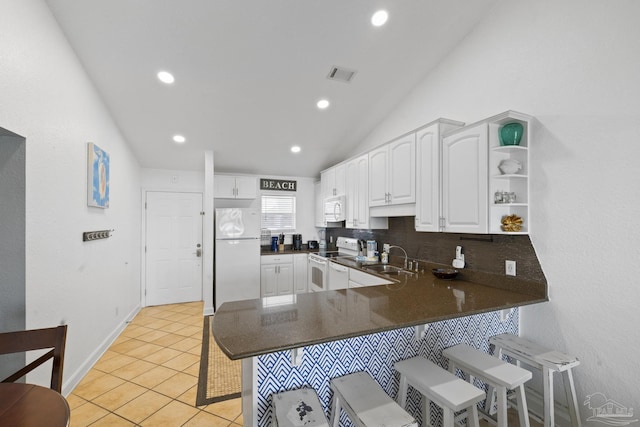 kitchen featuring vaulted ceiling, white cabinetry, a kitchen bar, kitchen peninsula, and white appliances