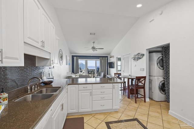 kitchen featuring vaulted ceiling, white cabinetry, sink, stacked washer and dryer, and kitchen peninsula