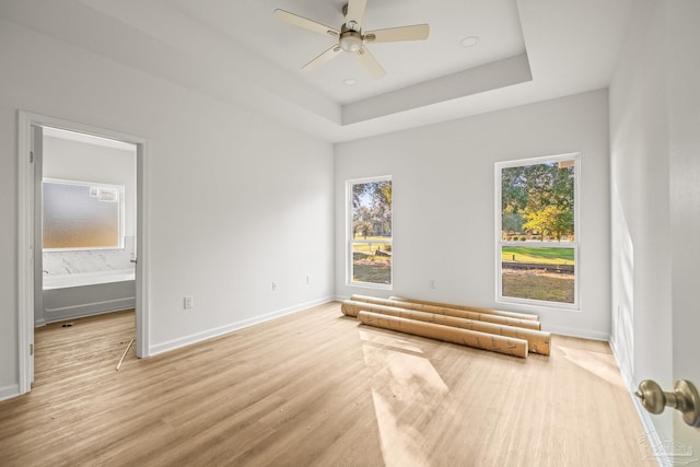 unfurnished bedroom with a raised ceiling, connected bathroom, light hardwood / wood-style flooring, and ceiling fan