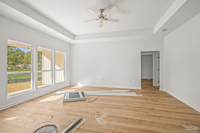 empty room with a raised ceiling, light hardwood / wood-style flooring, and ceiling fan