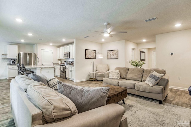 living room featuring ceiling fan, sink, a textured ceiling, and light wood-type flooring