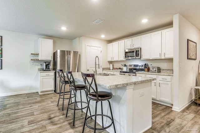 kitchen featuring white cabinetry, sink, stainless steel appliances, and a center island with sink