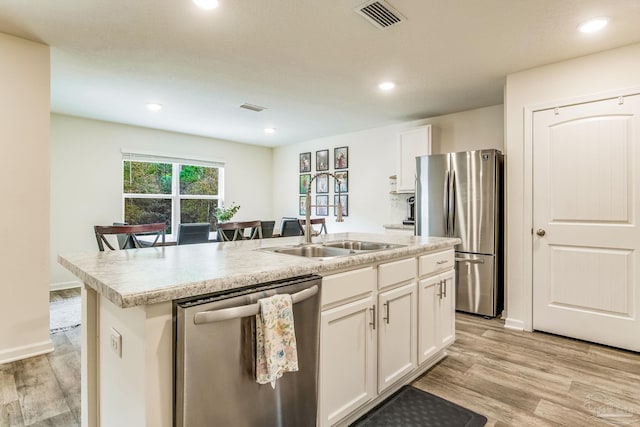 kitchen featuring sink, appliances with stainless steel finishes, light hardwood / wood-style floors, an island with sink, and white cabinets