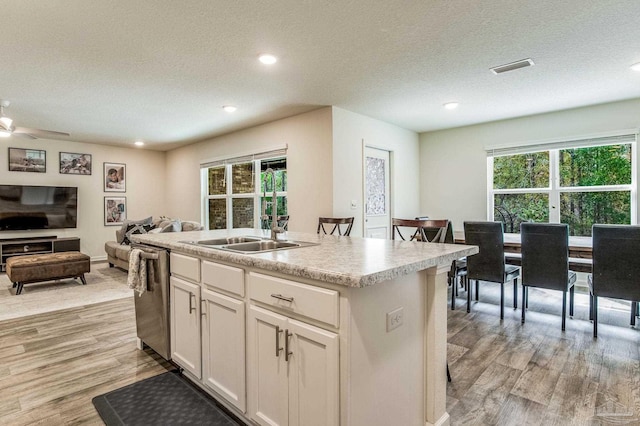 kitchen with white cabinetry, light hardwood / wood-style flooring, stainless steel dishwasher, and an island with sink