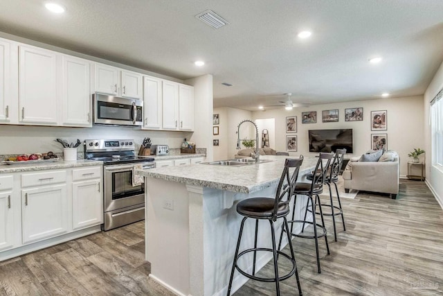 kitchen featuring stainless steel appliances, sink, a center island with sink, and white cabinets