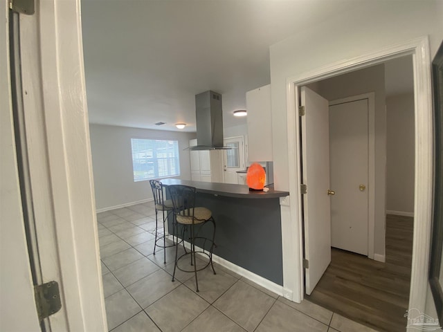 kitchen featuring light tile patterned floors, island exhaust hood, kitchen peninsula, a breakfast bar area, and white cabinets