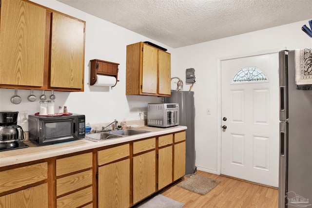 kitchen with sink, light hardwood / wood-style flooring, stainless steel refrigerator, fridge, and a textured ceiling