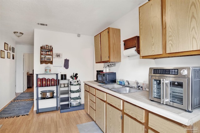 kitchen with sink, light hardwood / wood-style floors, a textured ceiling, and light brown cabinets