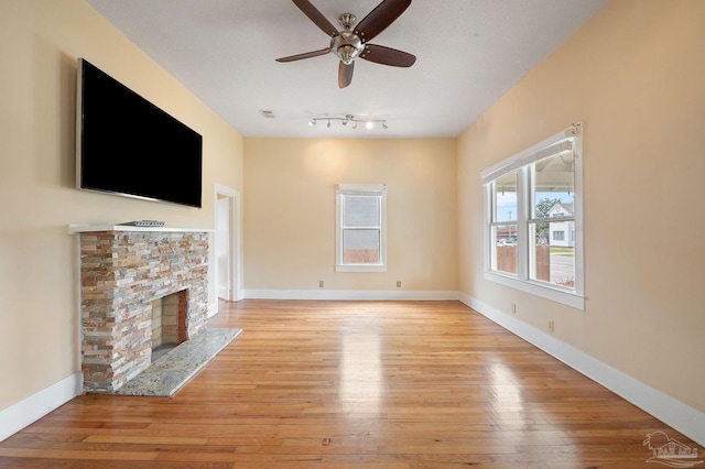 unfurnished living room with ceiling fan, a fireplace, and light hardwood / wood-style flooring