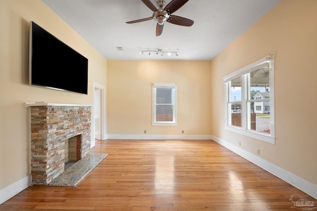 unfurnished living room featuring a stone fireplace, light hardwood / wood-style flooring, a textured ceiling, and ceiling fan