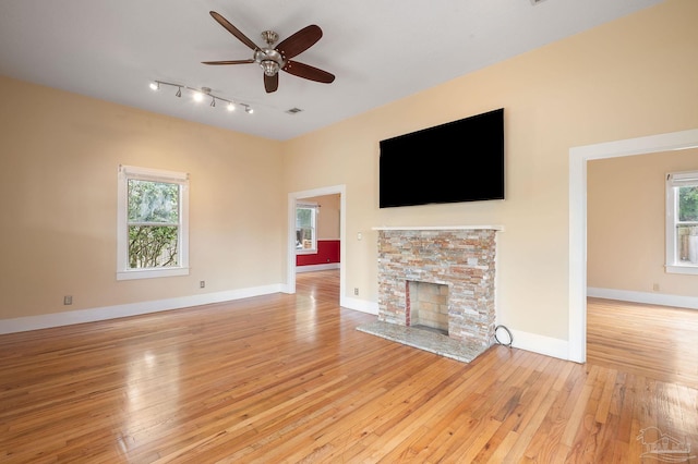 unfurnished living room with ceiling fan, a stone fireplace, and light wood-type flooring