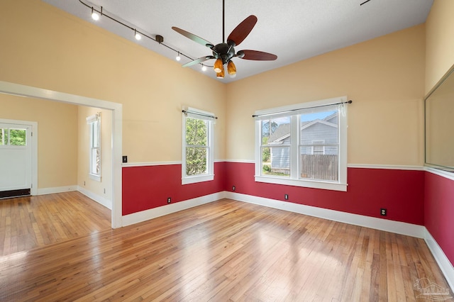 empty room featuring ceiling fan, track lighting, a textured ceiling, and light wood-type flooring