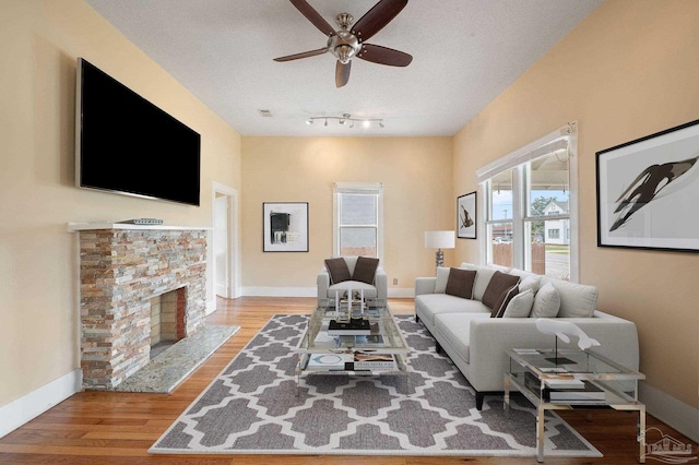 living room featuring ceiling fan, a fireplace, a textured ceiling, and light wood-type flooring