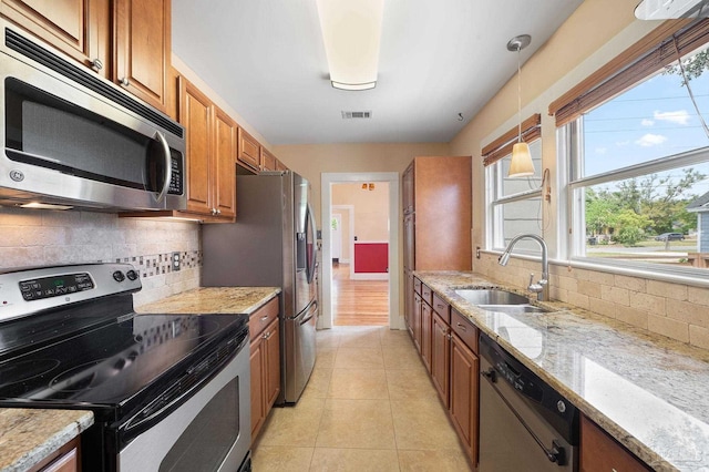 kitchen with pendant lighting, appliances with stainless steel finishes, light stone countertops, and sink