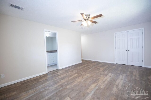 unfurnished bedroom featuring ensuite bath, ceiling fan, hardwood / wood-style flooring, and a closet