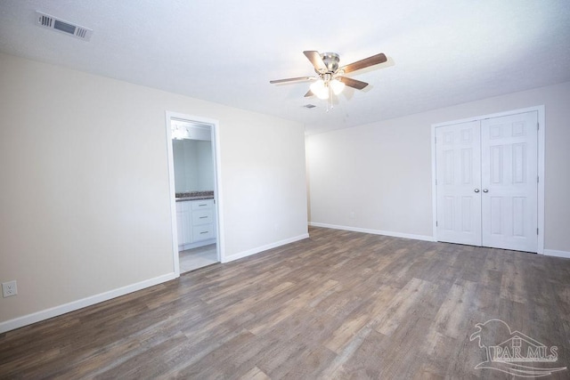 unfurnished bedroom with ensuite bath, dark wood-type flooring, ceiling fan, and a closet