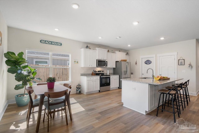 kitchen with white cabinets, a kitchen breakfast bar, stainless steel appliances, light hardwood / wood-style flooring, and a center island with sink