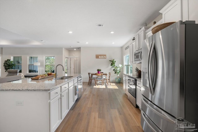 kitchen with light hardwood / wood-style flooring, stainless steel appliances, white cabinetry, and a kitchen island with sink