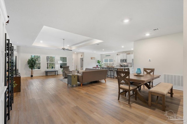 dining space featuring light wood-type flooring, a tray ceiling, and ceiling fan