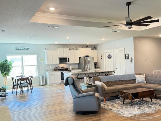 living room with ceiling fan, a textured ceiling, and light wood-type flooring