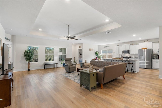 living room with light hardwood / wood-style flooring, a tray ceiling, ceiling fan, and a textured ceiling