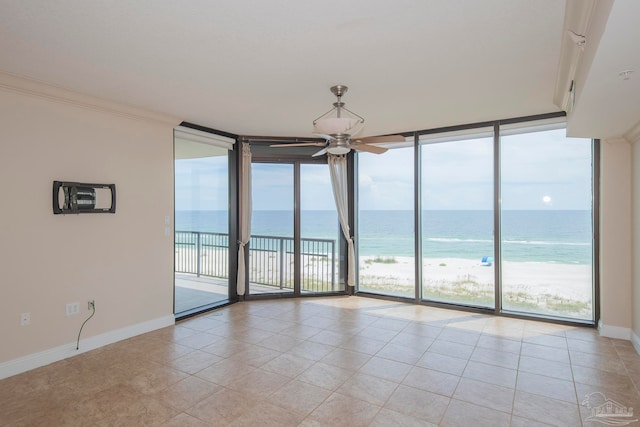 tiled empty room with a view of the beach, a water view, ceiling fan, and a wall of windows