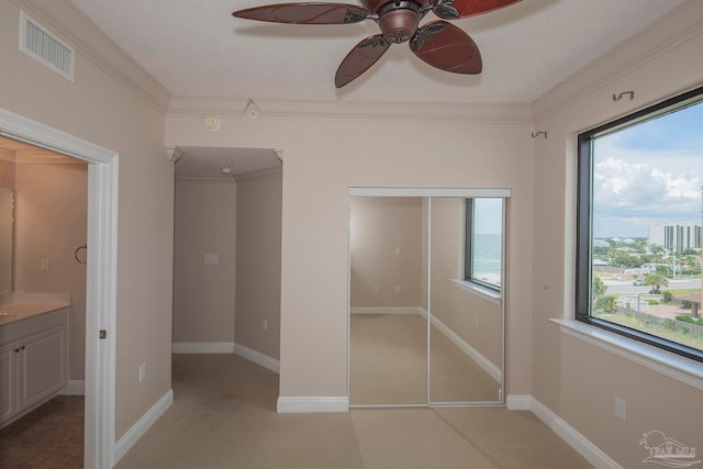 unfurnished bedroom with ornamental molding, light colored carpet, ensuite bath, and ceiling fan