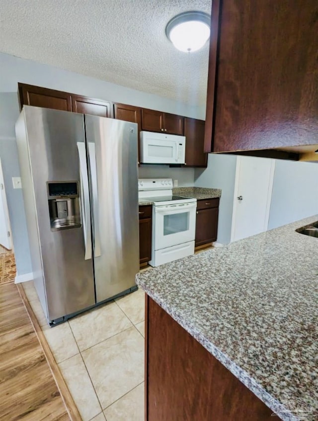 kitchen featuring light tile patterned floors, white appliances, dark brown cabinetry, light stone countertops, and a textured ceiling