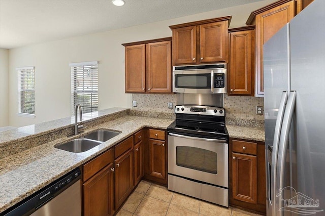 8868 Sanderling Ln, Navarre, FL 32566 - kitchen featuring appliances with stainless steel finishes, a sink, brown cabinets, light stone countertops, and light tile patterned flooring
