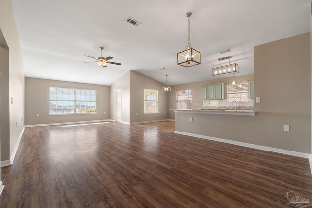 unfurnished living room with ceiling fan with notable chandelier, sink, lofted ceiling, and dark wood-type flooring