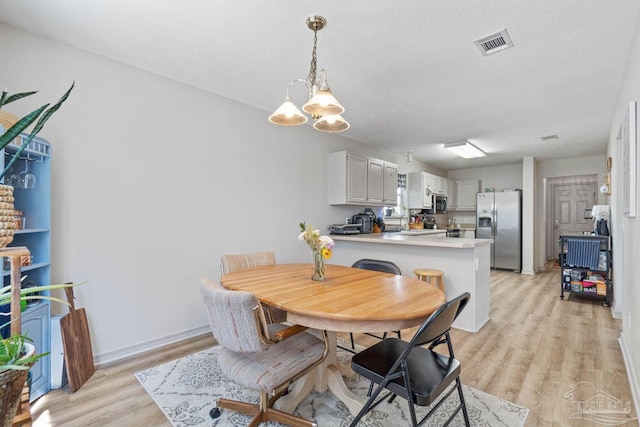 dining space featuring an inviting chandelier, a textured ceiling, and light hardwood / wood-style floors