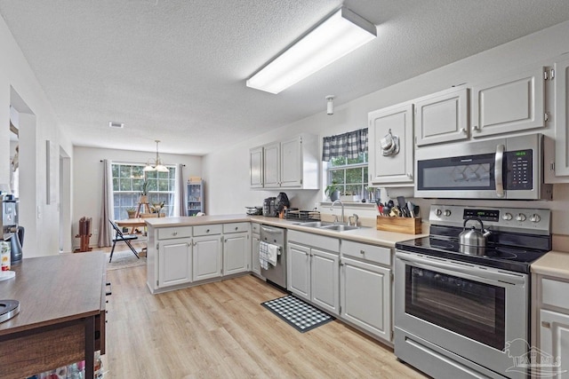 kitchen featuring hanging light fixtures, stainless steel appliances, kitchen peninsula, sink, and light hardwood / wood-style floors