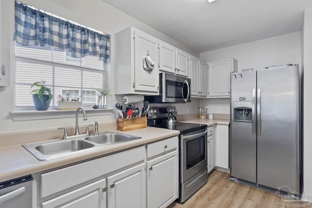 kitchen with sink, light wood-type flooring, white cabinetry, appliances with stainless steel finishes, and a textured ceiling