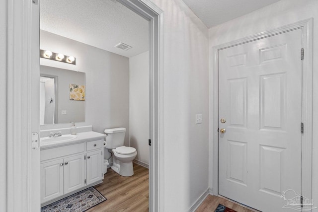 bathroom with vanity, toilet, wood-type flooring, and a textured ceiling