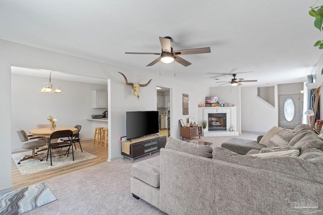 living room with a textured ceiling, a tiled fireplace, light hardwood / wood-style floors, and ceiling fan