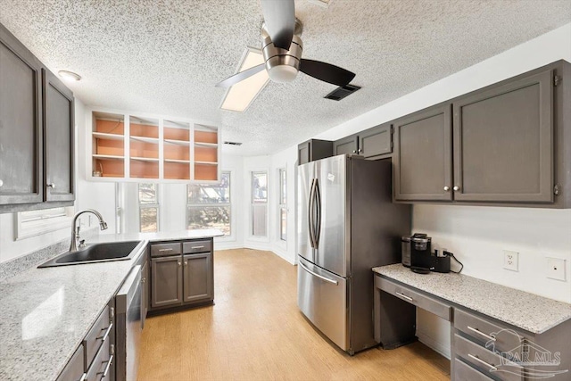 kitchen with light stone countertops, light wood finished floors, a sink, built in desk, and appliances with stainless steel finishes