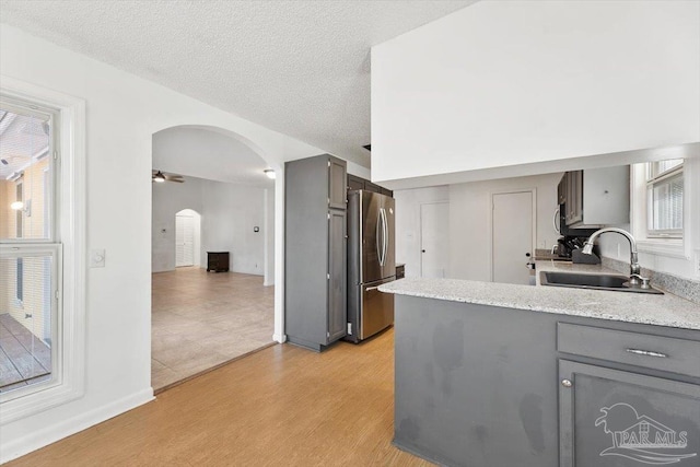 kitchen with a sink, arched walkways, gray cabinets, and freestanding refrigerator