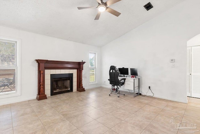 office featuring visible vents, baseboards, a tiled fireplace, vaulted ceiling, and a textured ceiling