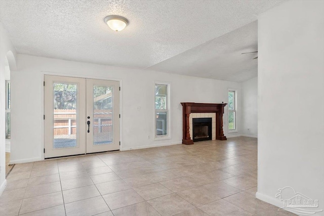 unfurnished living room featuring a tiled fireplace, light tile patterned flooring, french doors, and baseboards