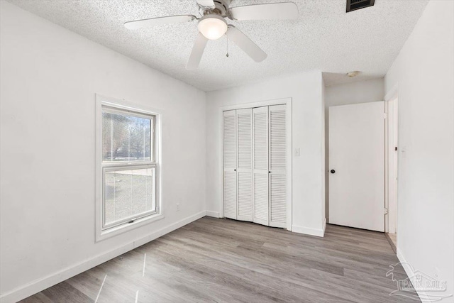 unfurnished bedroom featuring a textured ceiling, wood finished floors, a closet, and baseboards