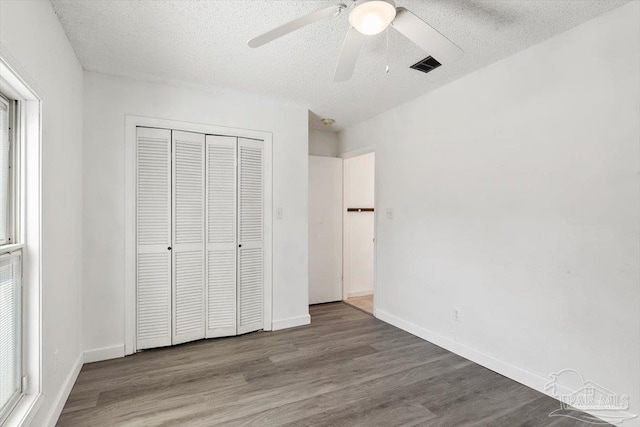 unfurnished bedroom with a closet, visible vents, a textured ceiling, and wood finished floors