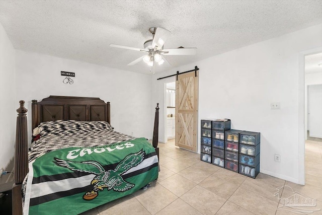 bedroom featuring tile patterned flooring, baseboards, a barn door, a textured ceiling, and a ceiling fan