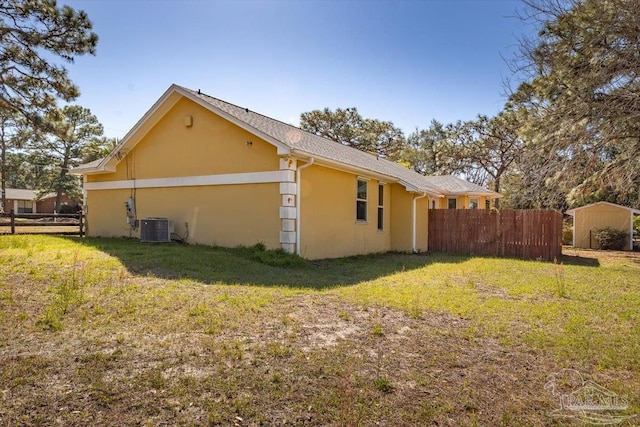 view of home's exterior featuring fence, central AC, stucco siding, an outdoor structure, and a lawn