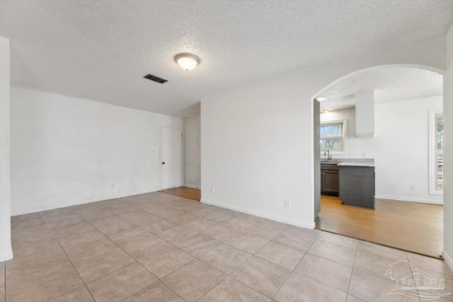 unfurnished room featuring visible vents, light tile patterned floors, arched walkways, a textured ceiling, and a sink