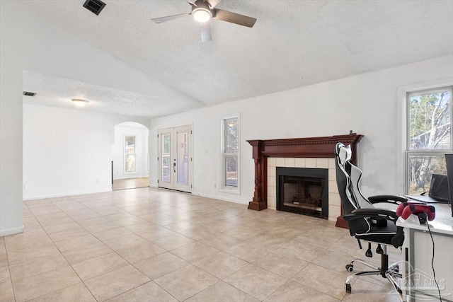 unfurnished living room featuring visible vents, a tiled fireplace, lofted ceiling, arched walkways, and a textured ceiling