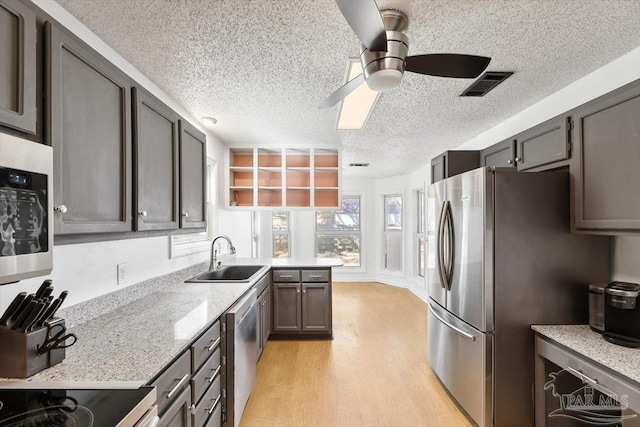 kitchen with visible vents, light wood finished floors, a peninsula, a sink, and appliances with stainless steel finishes