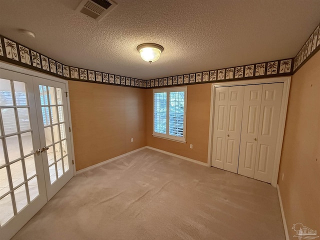 unfurnished bedroom featuring carpet flooring, a closet, a textured ceiling, and french doors